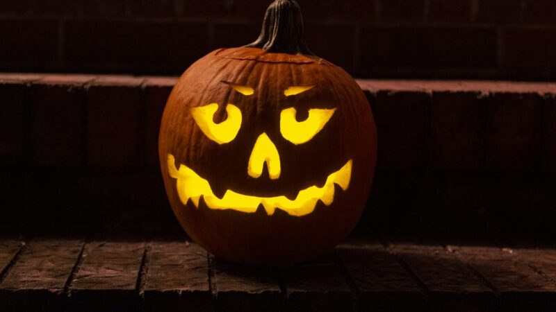 A carved jack o' lantern glowing with candlelight on brick front steps at night.
