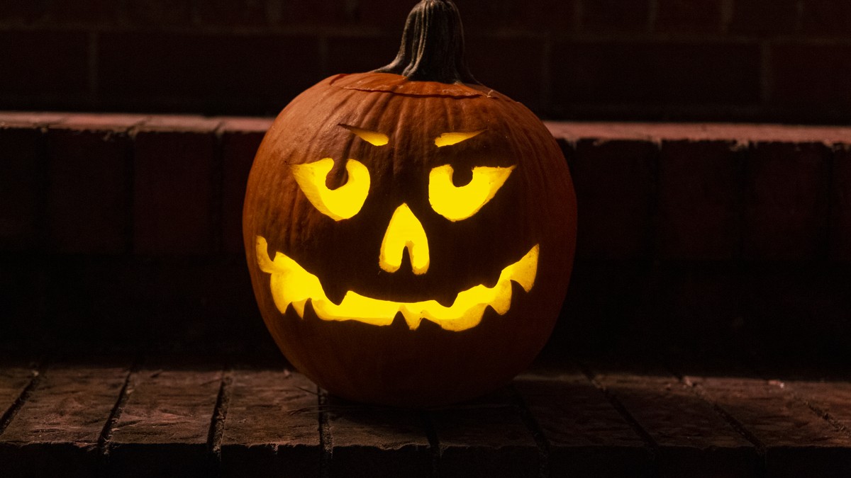 A carved jack o' lantern glowing with candlelight on brick front steps at night.
