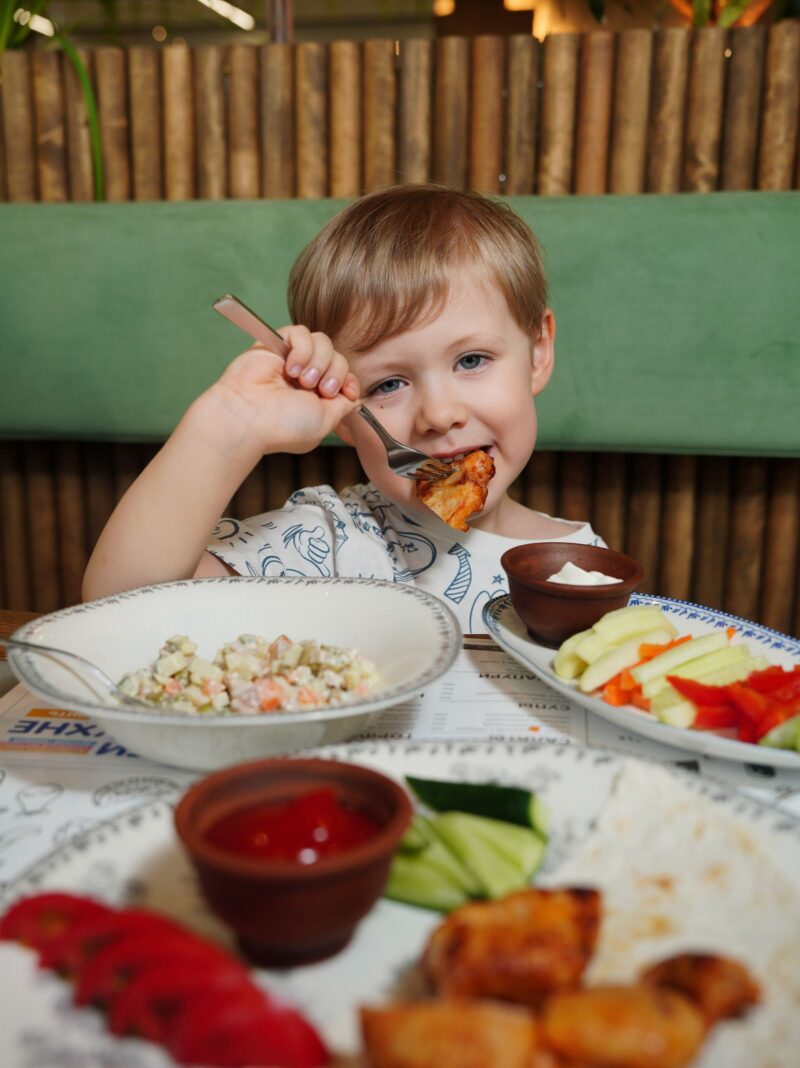 Young child happily eating a meal of fresh vegetables with dip at the table