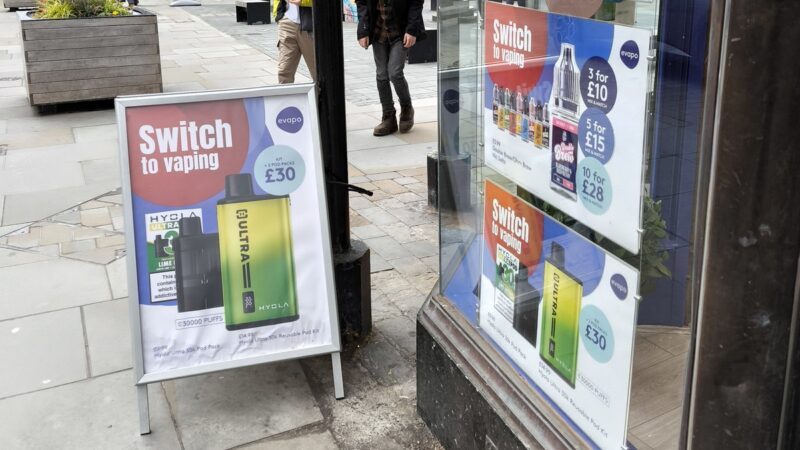 A UK high street vape shop window and pavement A board advertising disposable vapes and e-liquid deals, with signs reading Switch to vaping.