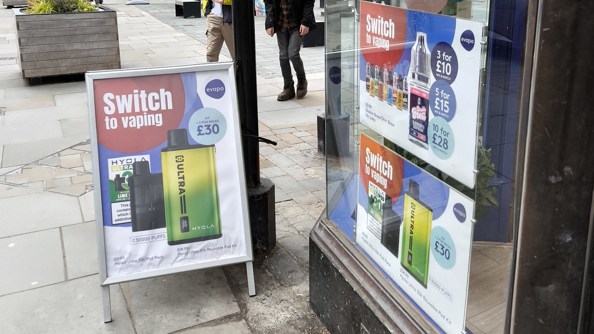 A UK high street vape shop window and pavement A board advertising disposable vapes and e-liquid deals, with signs reading Switch to vaping.